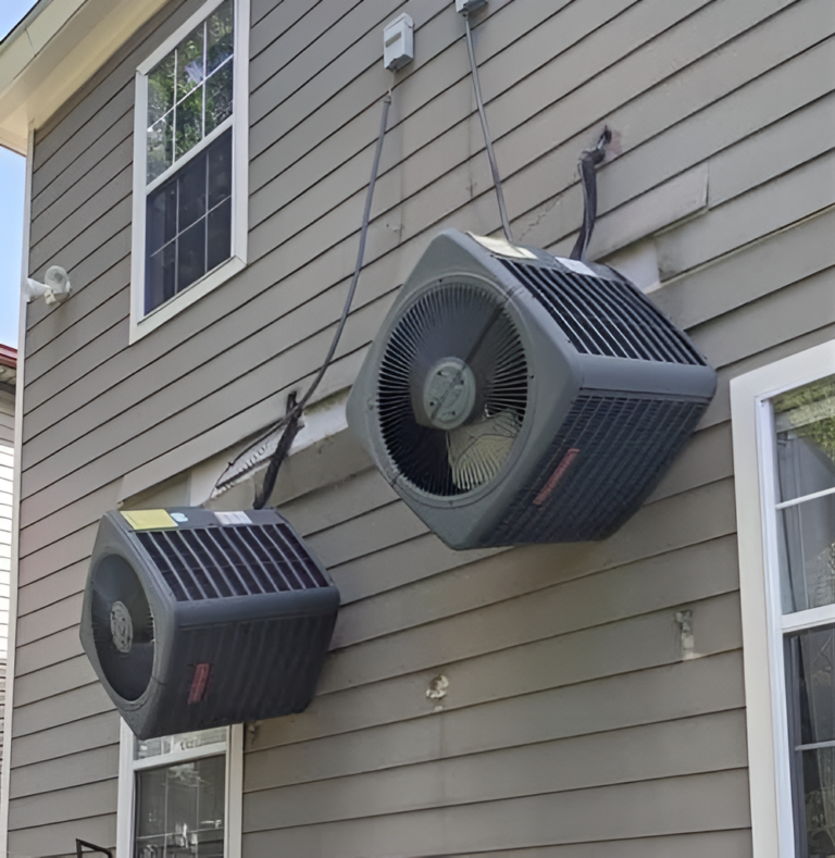 Two AC units mounted on the outside wall of a house.